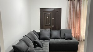 A modern living room with a sectional sofa, a dark wooden cabinet, and a fluffy rug. - 3-bed Apartment, Sleeps 6 With Wi-fi (Sakumono)