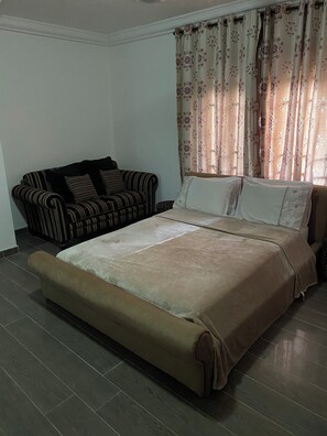 A bedroom with a bed, a sofa, and a window with curtains.