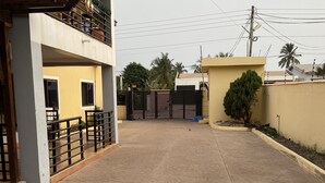 A gated residential area with a paved driveway leading to a building with a balcony. - 3-bed Apartment, Sleeps 6 With Wi-fi (Sakumono)
