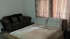 A room with a sofa, a patterned curtain, and a stack of folded blankets. - 3-bed Apartment, Sleeps 6 With Wi-fi (Sakumono)