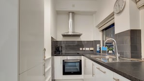 Una cuina moderna amb armaris blancs, una campana d'extracció d'acer inoxidable, un forn integrat i un taulell negre.