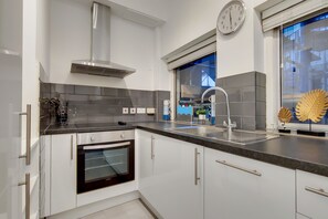 A modern kitchen with white cabinets, a stainless steel range hood, a built-in oven, a double sink, and a window with decorative leaf art.