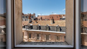 Blick aus einem Fenster auf ein Gebäude mit mehreren Dächern und einem klaren Himmel.