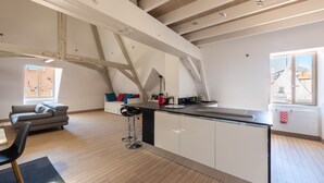 Ein modernes Loft mit freiliegenden Holzbalken, einer Kücheninsel, einer Couch und Blick auf die Stadt durch große Fenster.