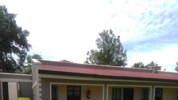 A building with a red roof and a small front porch. There are two small bushes in front of the building. - Juliana County Hotel (Bondo)