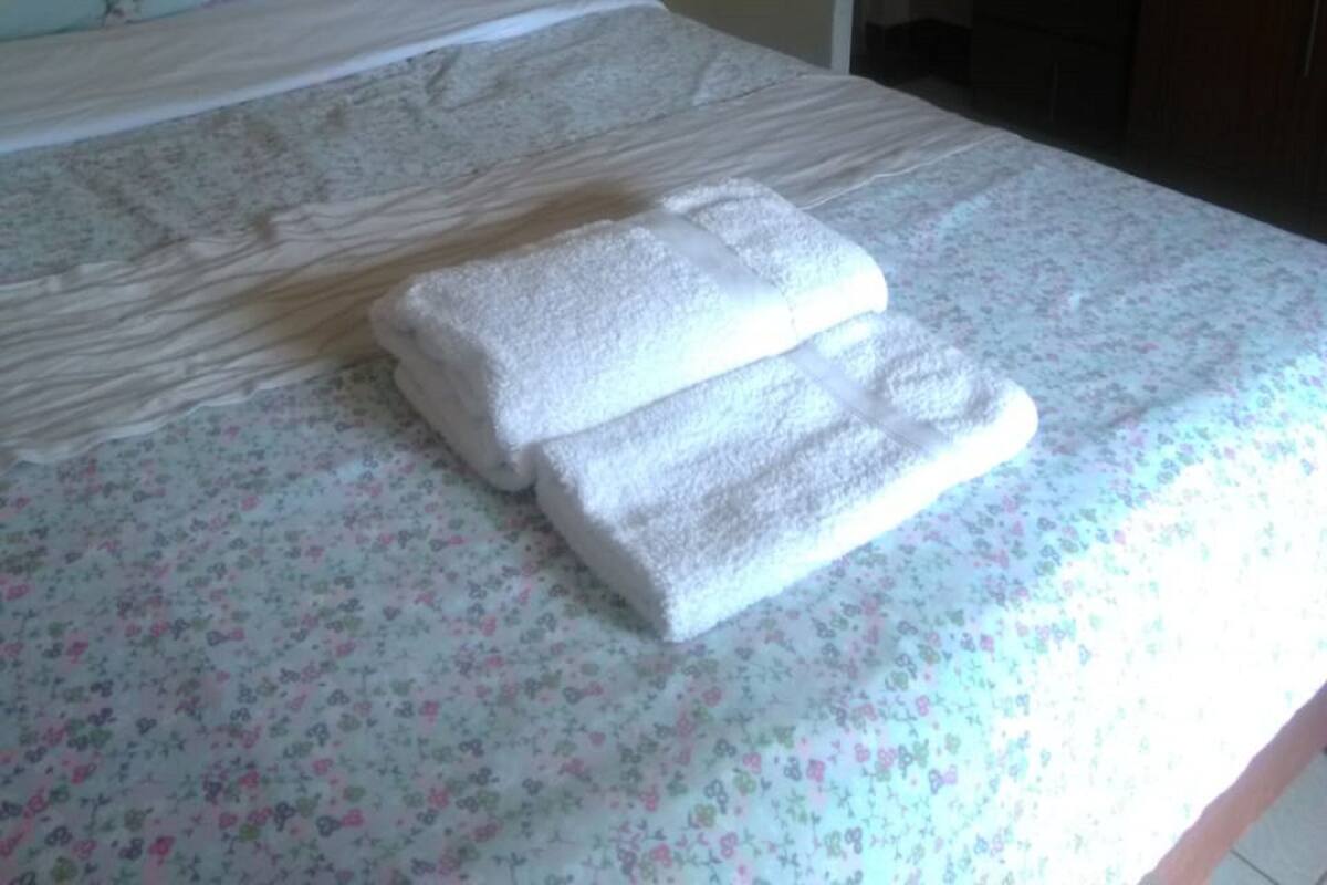 Una cama con cubrecama floral, dos toallas blancas dobladas y un cabecero de madera.