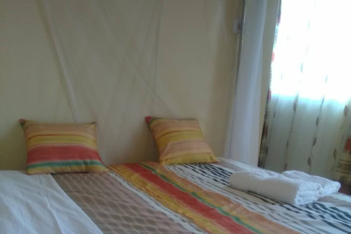Una cama con ropa de cama a rayas y dos almohadas, una ventana con cortinas y una pared lisa.