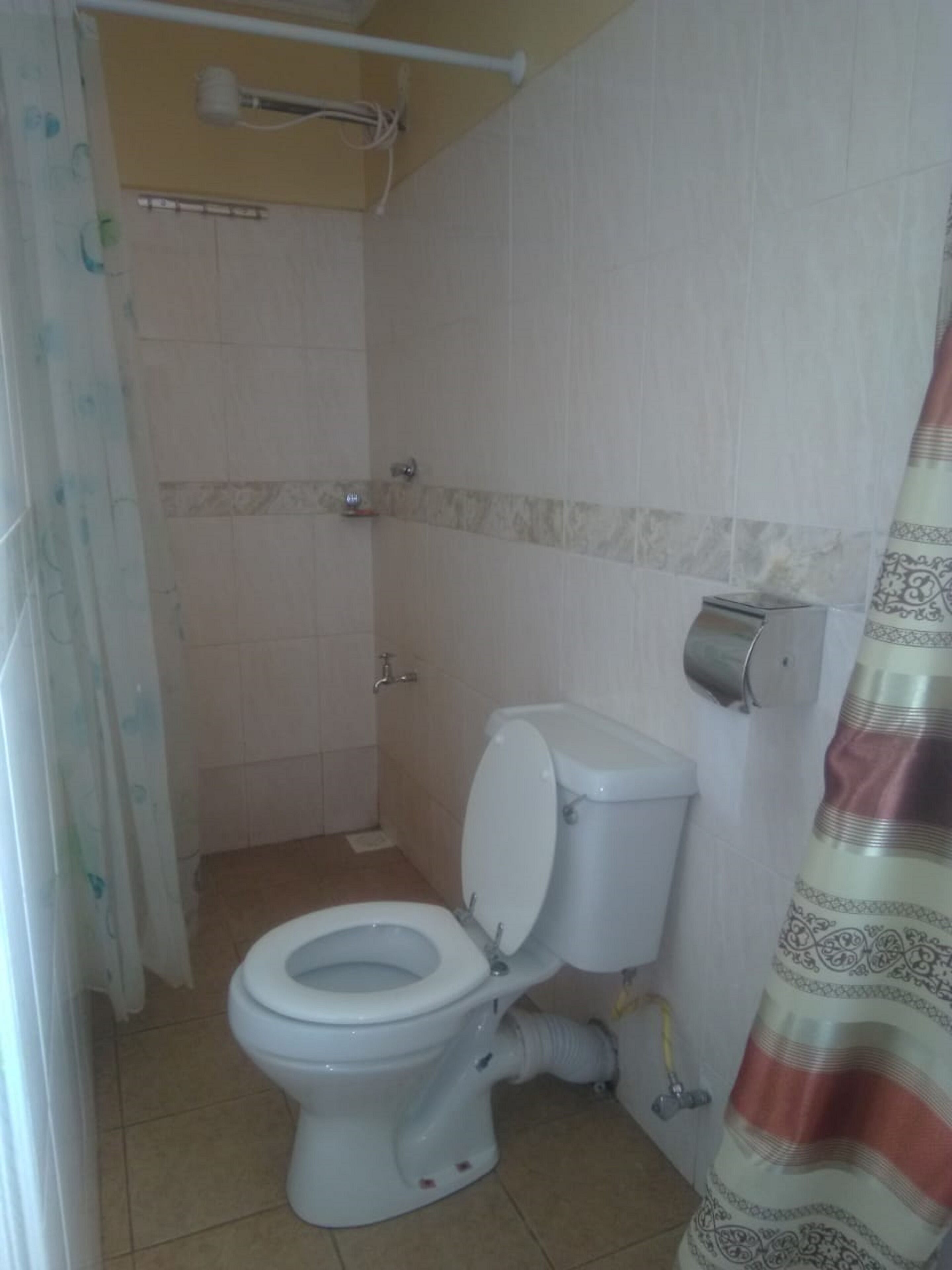 A small bathroom with a toilet, a shower, and a towel dispenser.