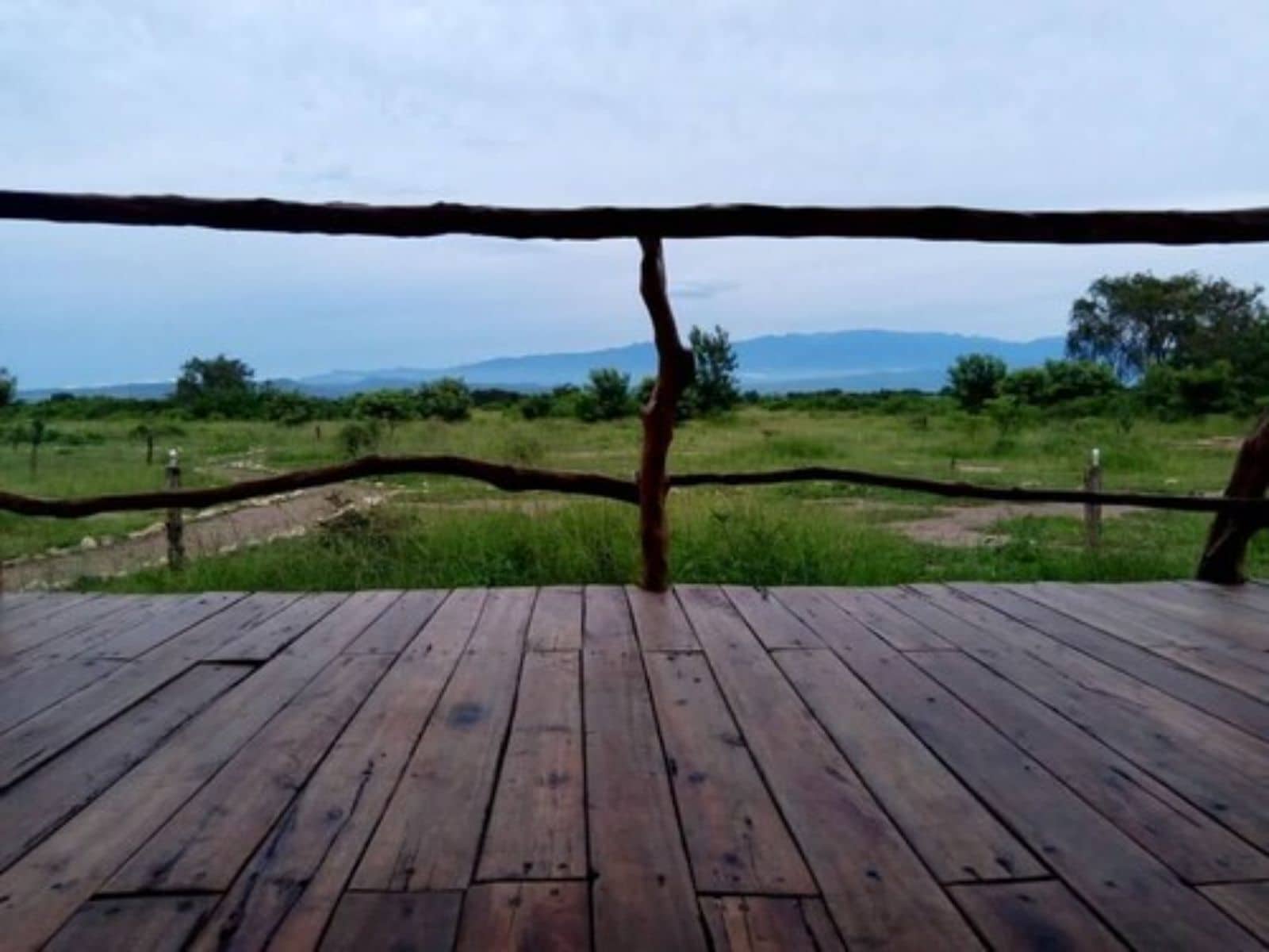 A wooden deck with a view of a grassy landscape and distant mountains.