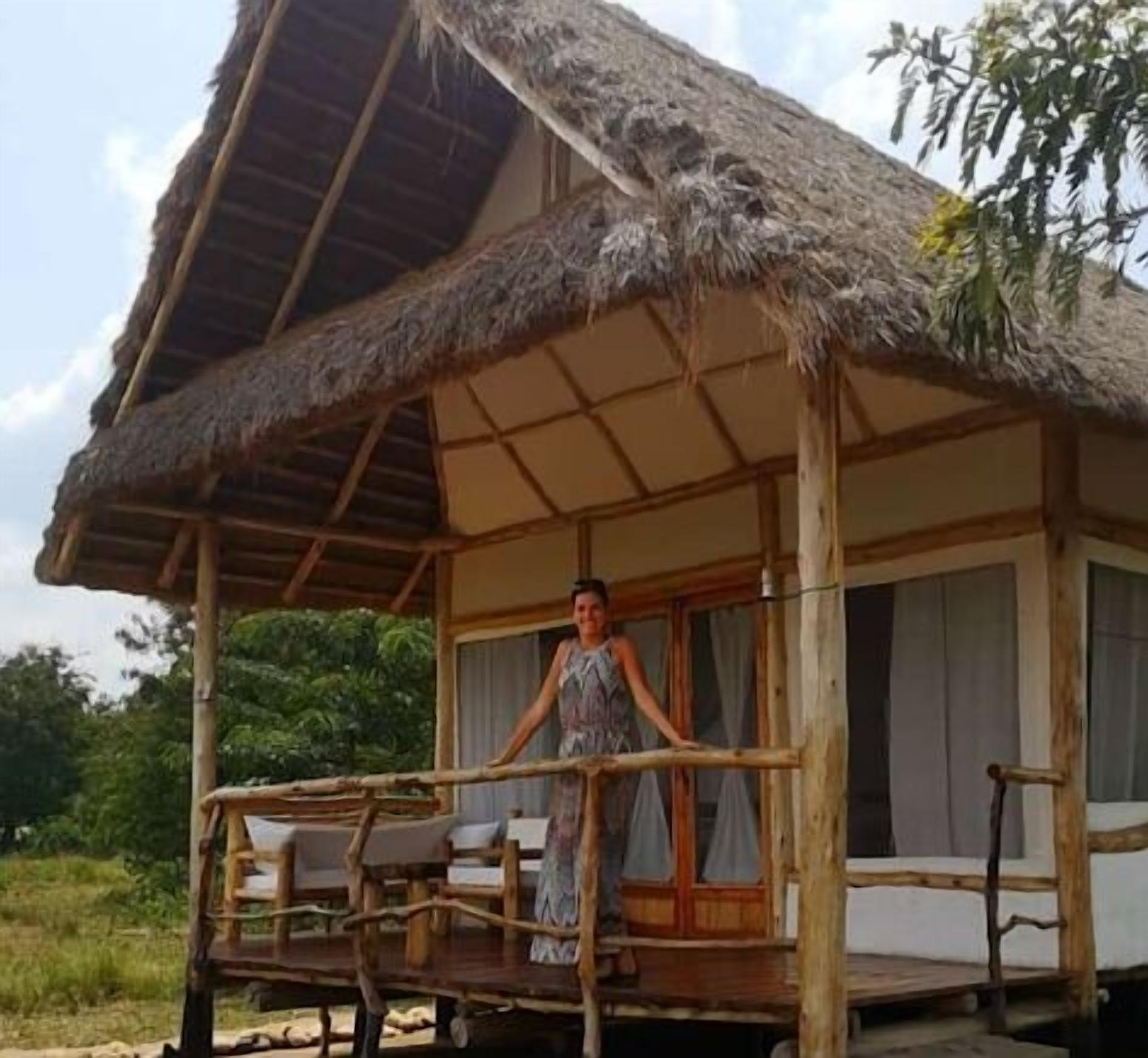 Een rieten bungalow met houten balkon, één raam en een deur.