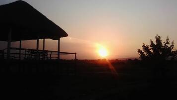 A structure with a roof, possibly a pavilion or shelter, in a natural setting with a sunset in the background.