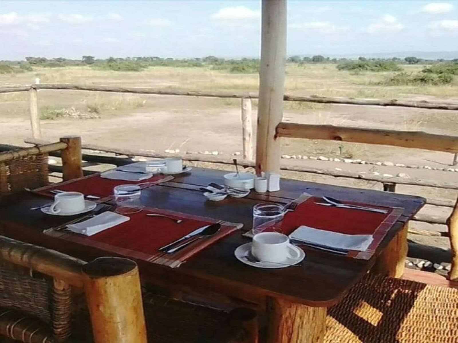 Un espace de restauration en plein air avec une table dressée pour deux personnes, entouré d’une clôture en bois, donnant sur un paysage verdoyant.