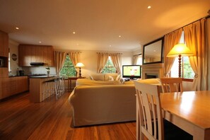 Cozy living space with a central seating area, dining table, and mounted TV. Enjoy a fireplace and kitchen with cabinets and countertop.