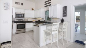 A modern kitchen with white cabinetry, stainless steel appliances, and a central island with bar stools.