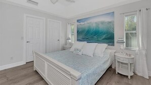A bedroom with a bed, a ceiling fan, a window with curtains, and a wall painting.