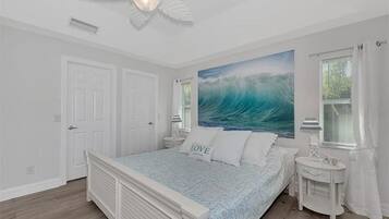 Une chambre à coucher avec un lit, un ventilateur de plafond, une fenêtre avec des rideaux et un tableau au mur.