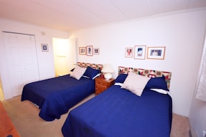 A hotel room with two beds, a nightstand, a lamp, and framed pictures on the wall.