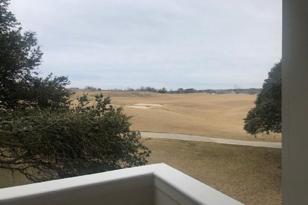 Vista de uma varanda com vista para um vasto campo aberto, com árvores esparsas e céu nublado.