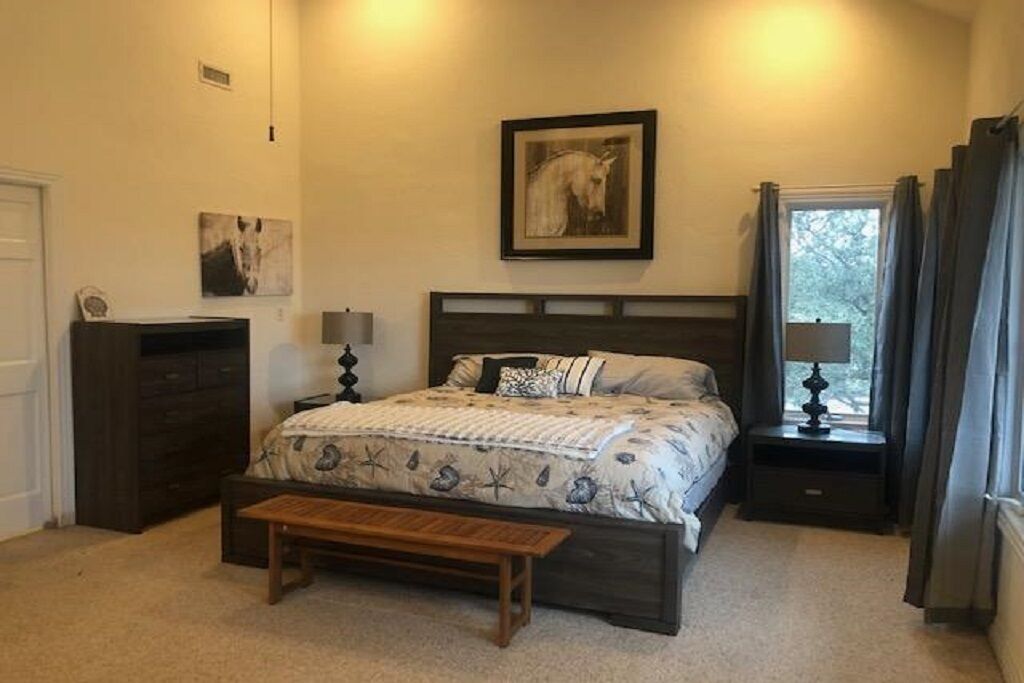 A bedroom with a bed, a nightstand, a bench, a dresser, and a window with curtains.