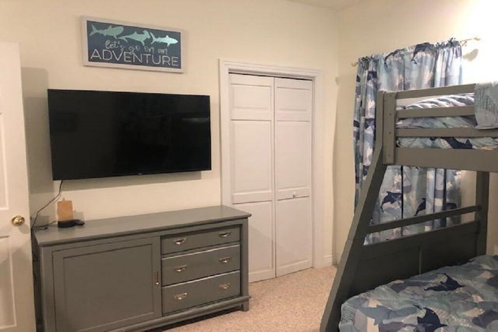 A bedroom with a bunk bed, a television on a dresser, a door, and a wall sign.