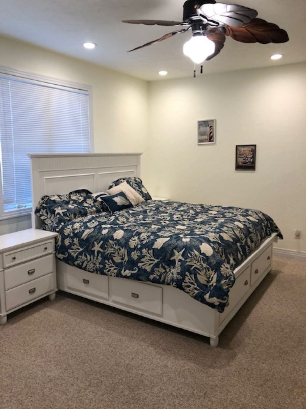 A bedroom with a bed, nightstands, a ceiling fan, and a window with blinds.