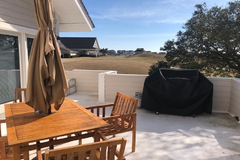 Une terrasse avec une table et des chaises en bois, un barbecue et une vue sur un quartier résidentiel.