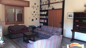 A cozy living room with a sofa, armchair, and a coffee table. There is a bookshelf filled with books and a door with a mirror.
