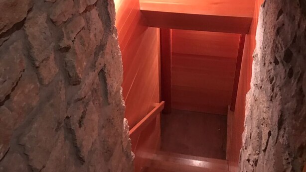 A wooden staircase in a stone-walled alcove with a red light fixture.