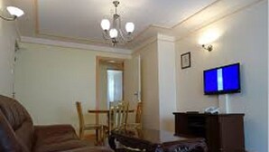 A living room with a brown leather sofa, a wooden dining table with chairs, a television mounted on the wall, and a chandelier. - Lighthomez Pinnacle Suites (Nairobi)