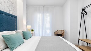 Un dormitorio ordenado con una cama grande, una silla y una mesita.