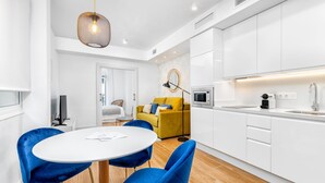 Una cocina moderna con armarios blancos, un sofá amarillo y sillas azules alrededor de una mesa blanca.