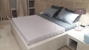 En seng med grå madras og puder, et natbord med lampe, og et garderobeskab med spejl.