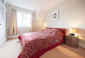Een slaapkamer met een groot bed, een nachtkastje met een lamp, een raam met gordijnen en een lijst met een afbeelding aan de muur.