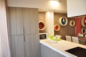 A modern kitchen with a built-in microwave, a sink, and a stove. There are colorful circular wall decorations and a wooden cabinet.