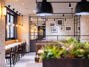 Interior moderno de restaurante com paredes de tijolo aparente, iluminação pendente e quadros nas paredes.