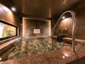 A hot spring bath with clear water, a metal ladder, and a temperature display.