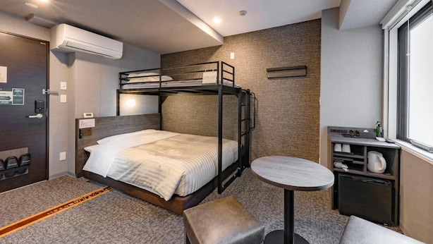A bunk bed room with a small table and bench, a window, and an air conditioning unit. - Super Hotel Ikebukuro Nishiguchi (Tokyo)