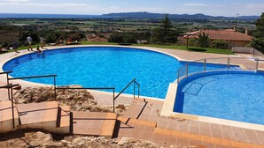 Uma piscina grande e translúcida em azul, com vista para colinas distantes e um céu claro.