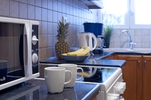 A kitchen with a microwave, two white mugs, a bowl with bananas and a pineapple, and a coffee maker. - Comfortable Apartment At The Foot of The Odeon of Herodes Atticus (Athens)