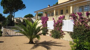 A Mediterranean-style building with a tiled roof, a balcony with white shutters, and a garden with palm trees and bougainvillea. - Villa Urgell - L'Estartit, Torre Vella (Estartit (L´))