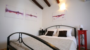 Ein Schlafzimmer mit einem Bett, einem Nachttisch, einem roten Beistelltisch und abstrakter Wandkunst.