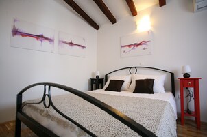 Quarto com cama, mesa de cabeceira, mesa lateral vermelha e arte abstrata na parede.