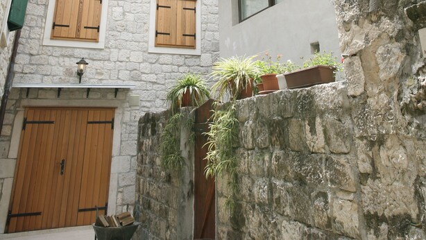 Eine enge Straße mit Steinhäusern, Holzhokken und einem kleinen Gartenbereich mit Blumentöpfen.