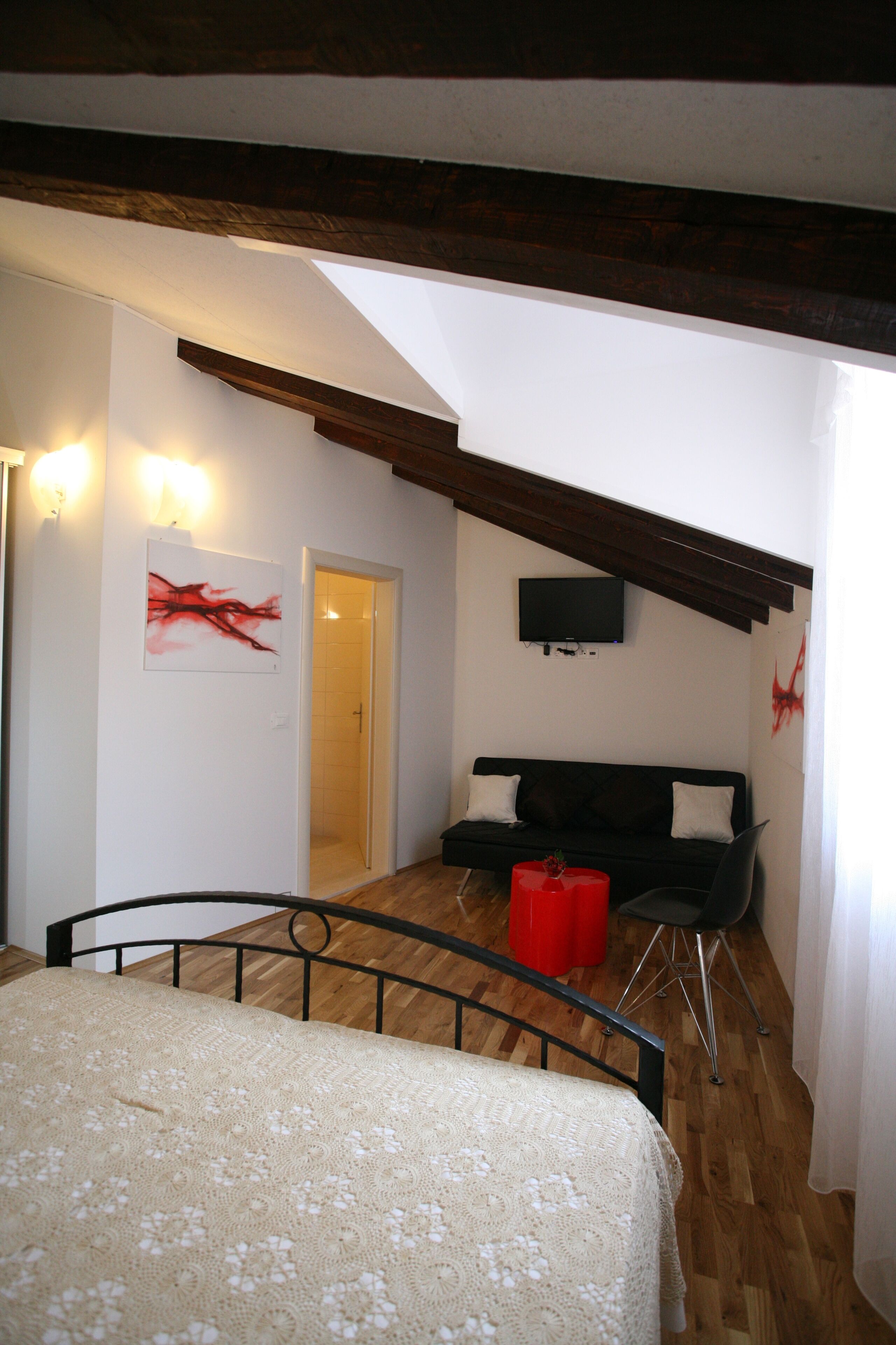 A bedroom with a bed, a black sofa, a red stool, a television, and a painting on the wall.