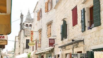 A narrow street with stone buildings, shops, and a variety of signs including a pizza place and a grill.