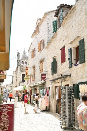 A narrow street with stone buildings, shops, and a variety of signs including a pizza place and a grill. - Rooms Beljan (Trogir)