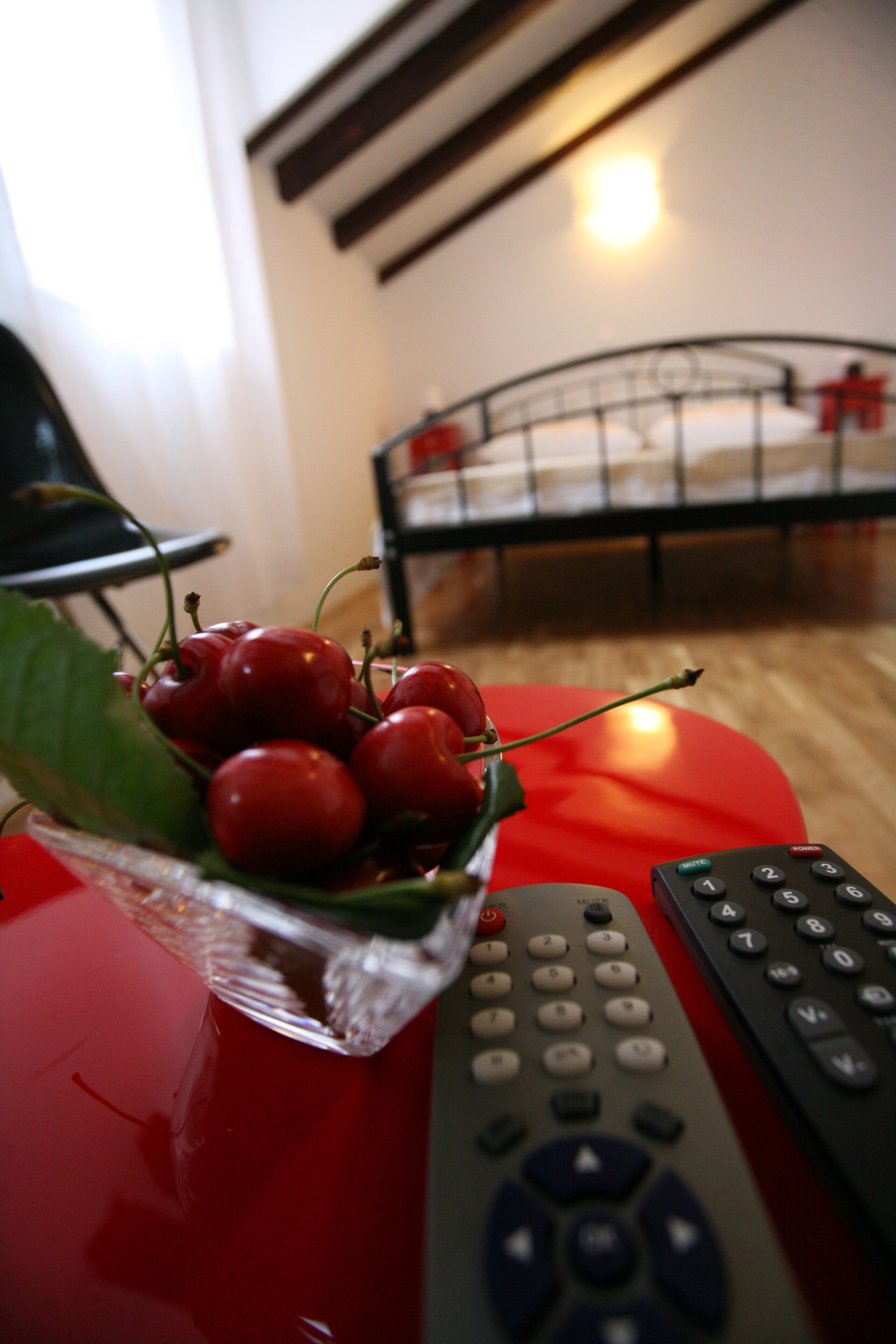 Una mesa roja con un bol de cerezas y dos controles remotos.