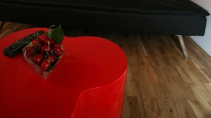 Ein modernes Wohnzimmer mit einem schwarzen Sofa, einem roten Couchtisch und einem an der Wand befestigten Flachbildfernseher.