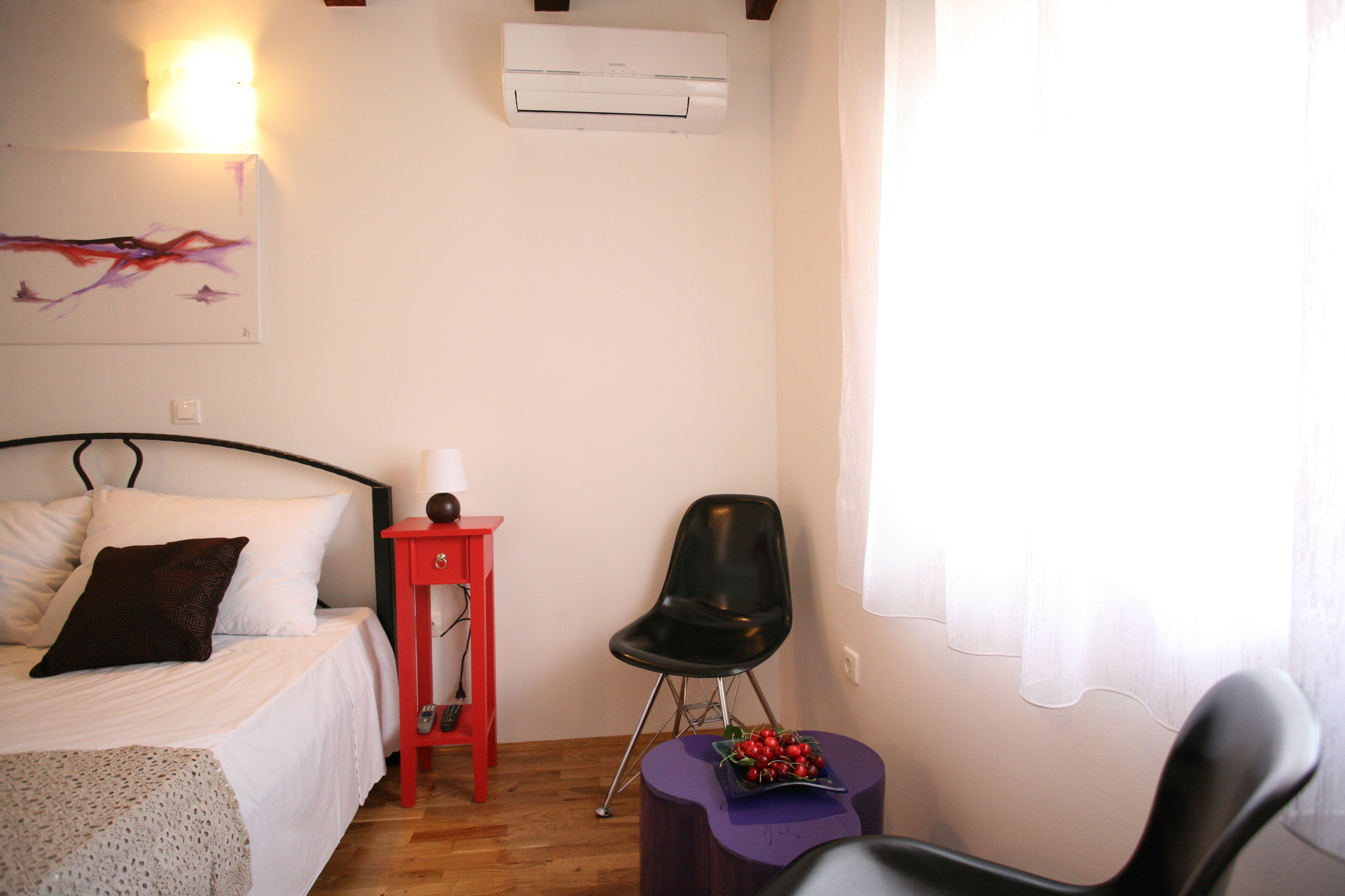 Un dormitorio con una cama, una mesita de noche roja, una silla negra y un aire acondicionado instalado en la pared.
