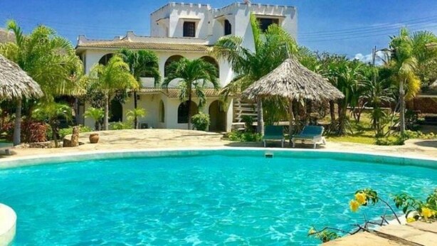A pool area with a clear blue pool, surrounded by palm trees and thatched umbrellas. - Lighthomez Villa Resort (Mombasa)